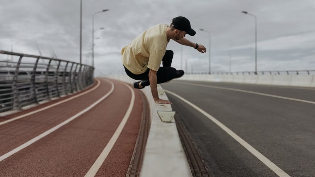 Young man performing parkour on a modern urban bridge railing with focus and agility.